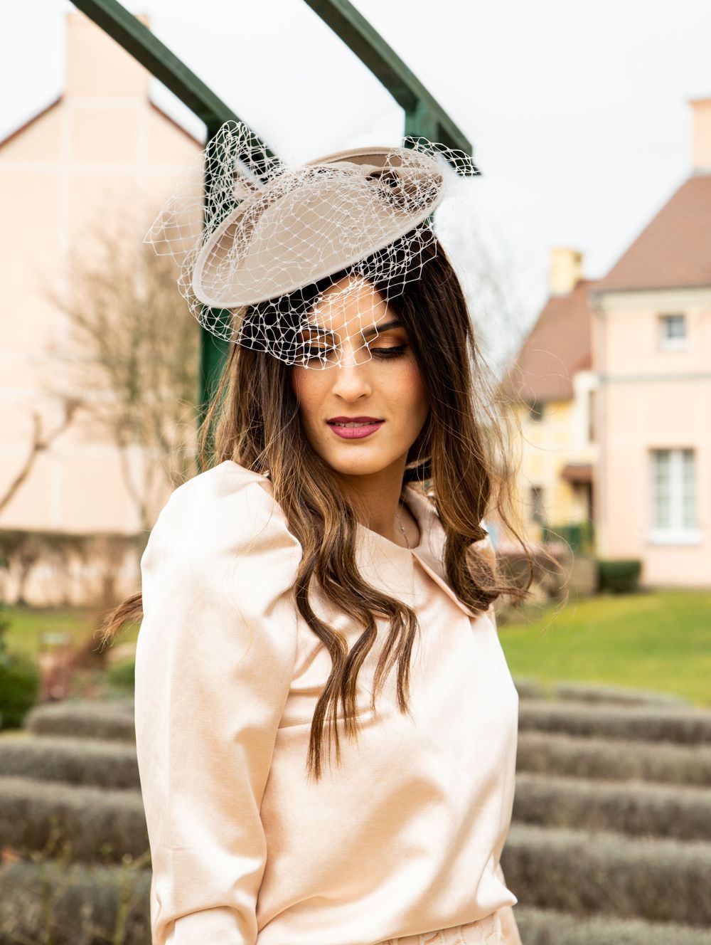 Elegant cream fascinator hat with netting detail styled in a romantic garden setting.