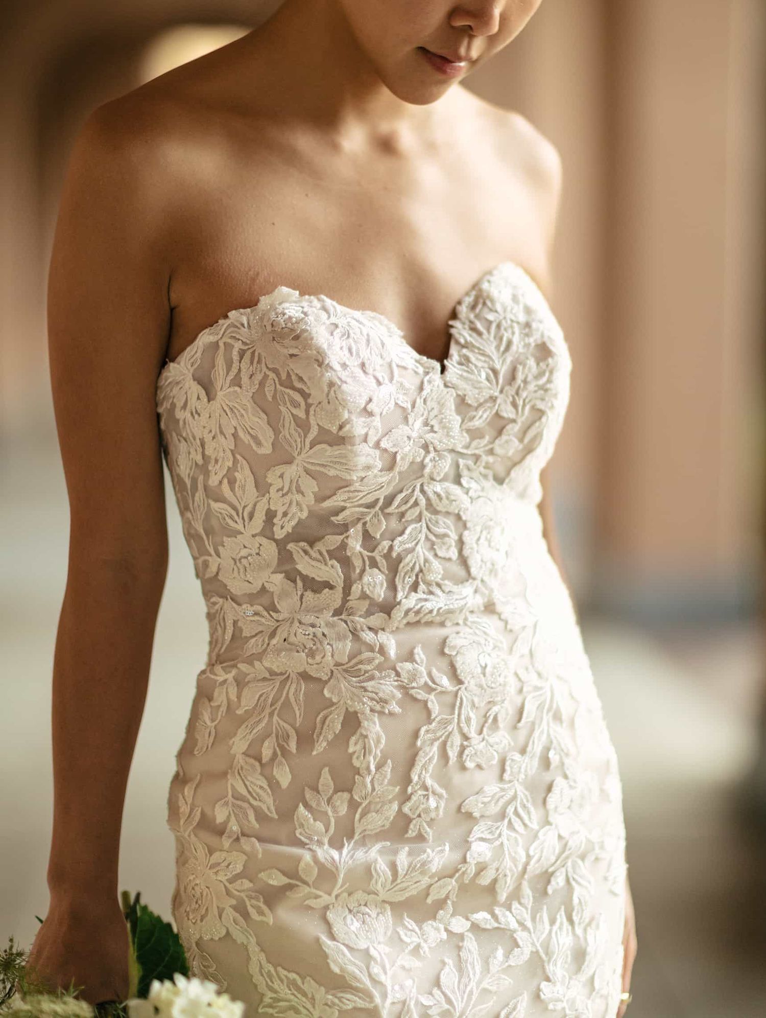 Close-up of bride in strapless sweetheart neckline wedding gown with raised floral lace embroidery.