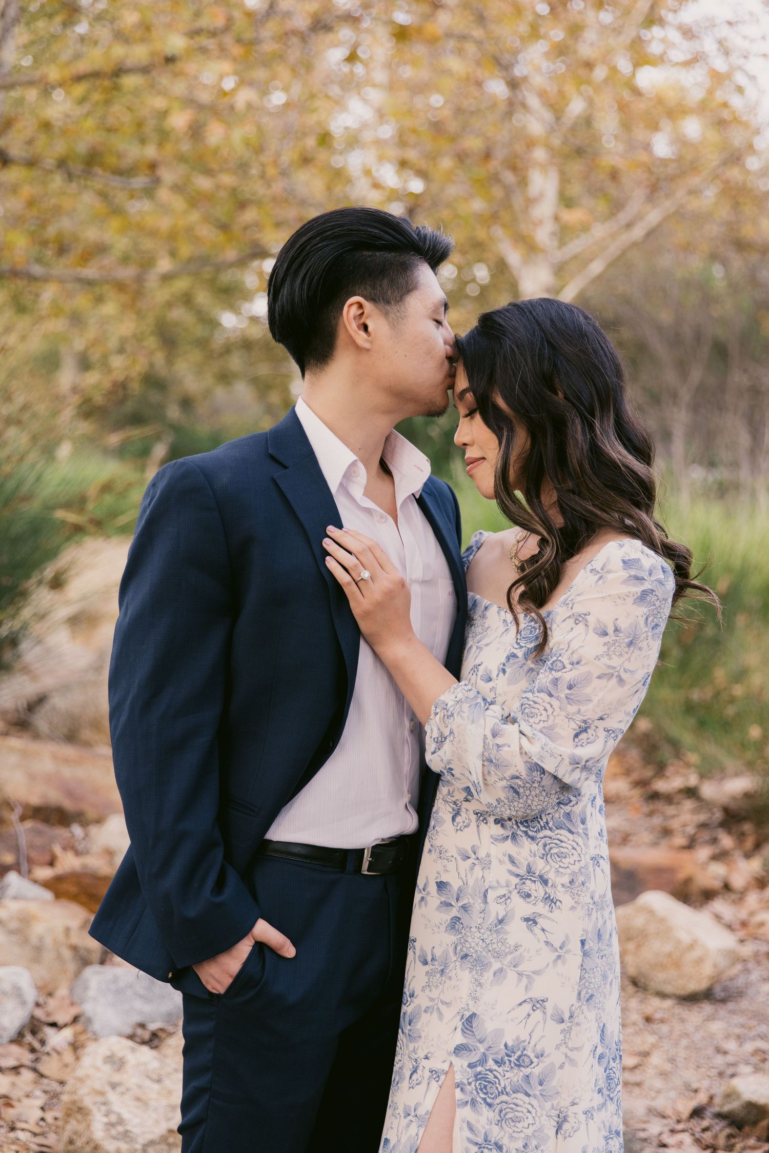 A romantic moment captured between two people in formal attire against a natural autumn backdrop.