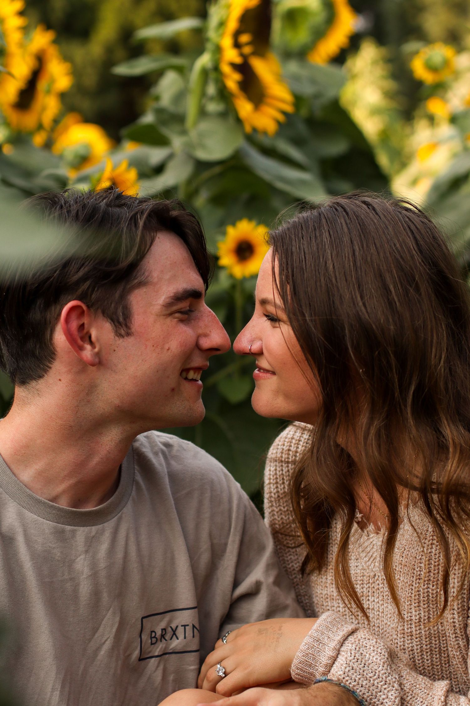 Couple sharing romantic moment in front of sunflower garden at sunset.