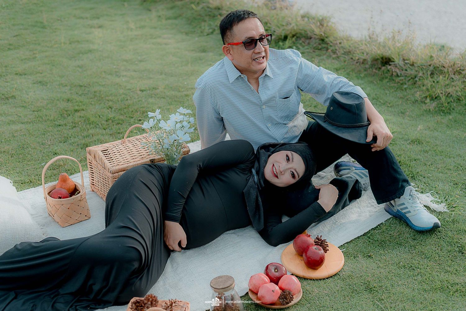 Couple having picnic on blanket with fruit basket and mountain scenery.