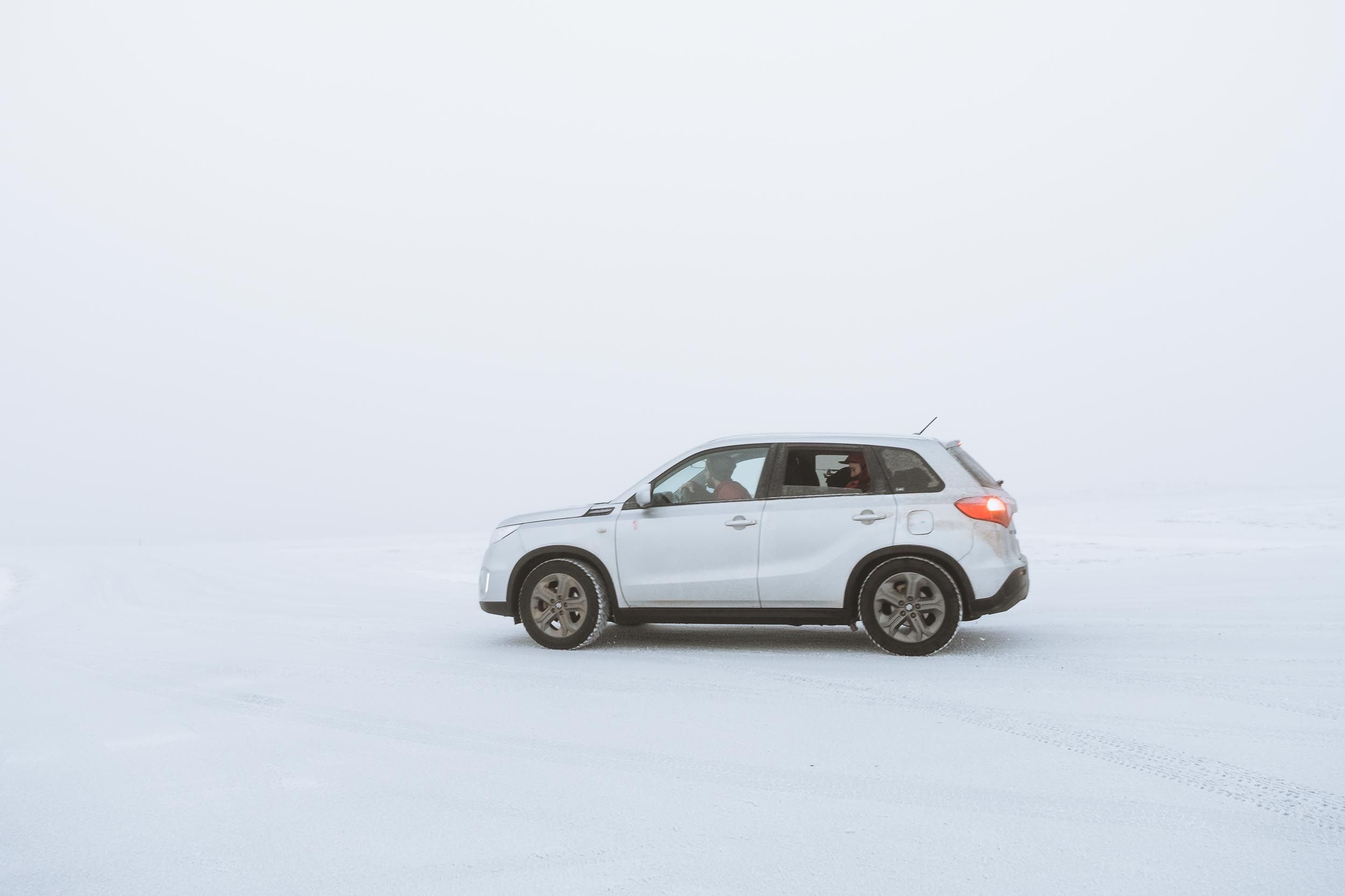 White SUV driving through a snowy winter landscape on a desolate road.
