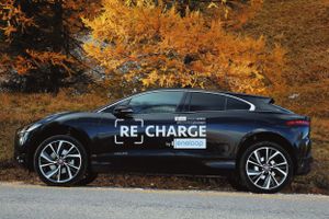 Black luxury sports car parked on road with vibrant autumn foliage in background during golden hour.