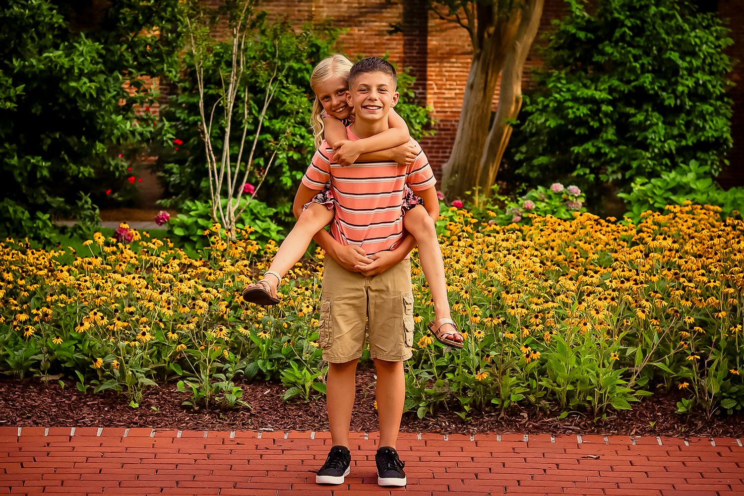 Young boy giving a little girl a piggyback ride in front of yellow flowers.