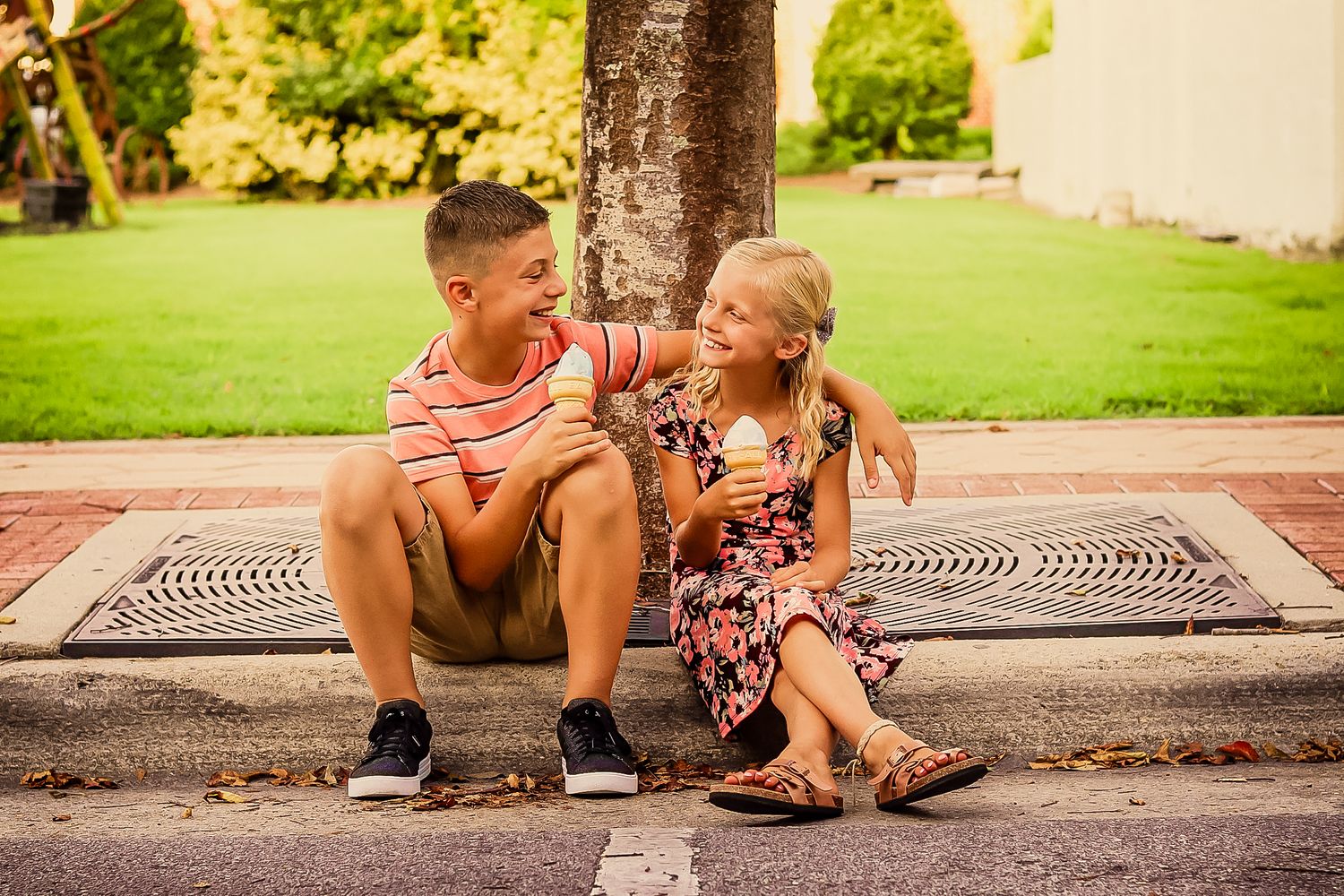 Brother and sister sitting together by a tree on a sunny day.