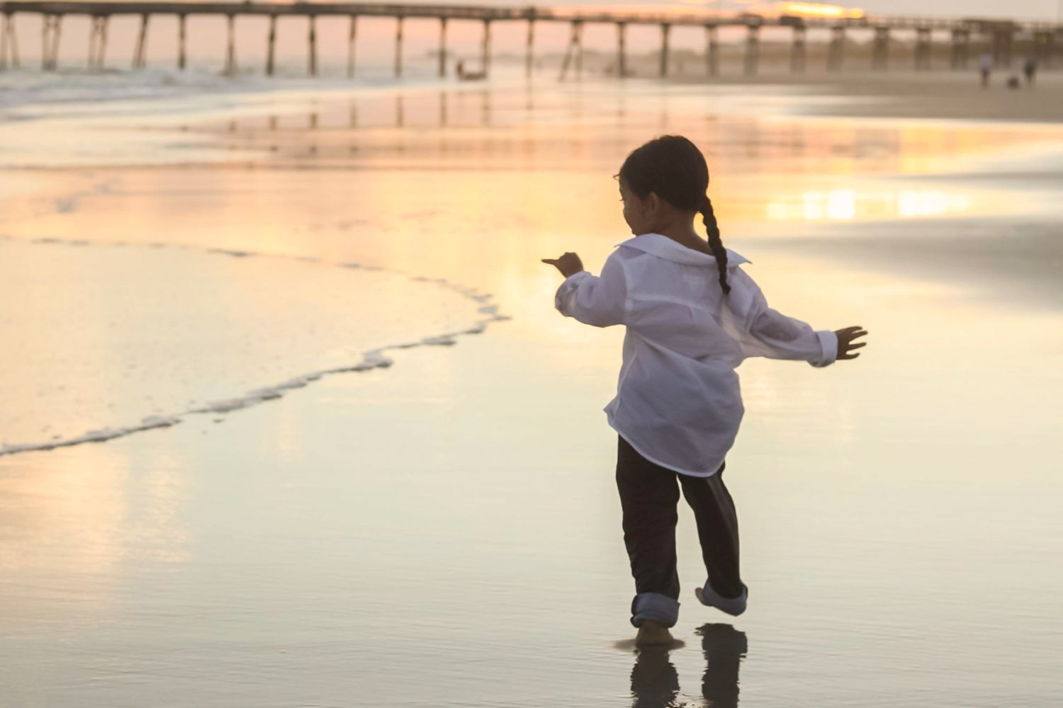 Young girl in white shirt standing at the ocean shore during a beautiful sunset.