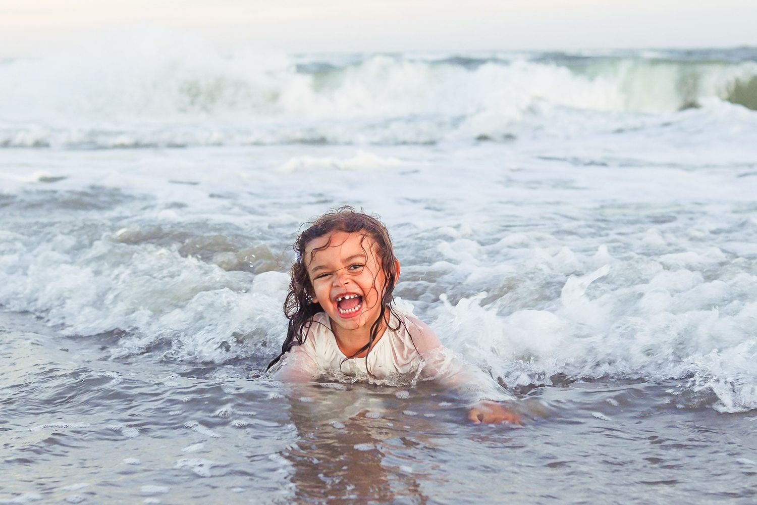 Laughing young girl playing in ocean waves at the beach.