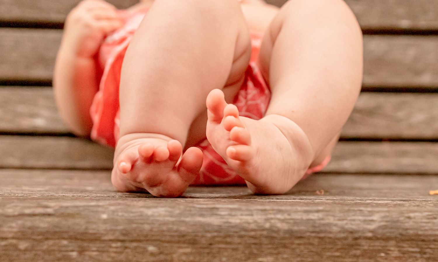 Close-up of adorable baby feet on a wooden surface, with a pink outfit visible.