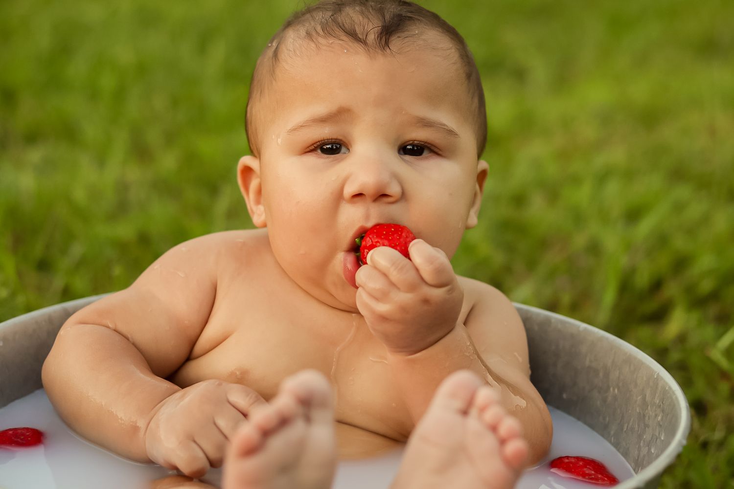 Adorable baby chewing on a fresh strawberry while sitting in an outdoor tub.