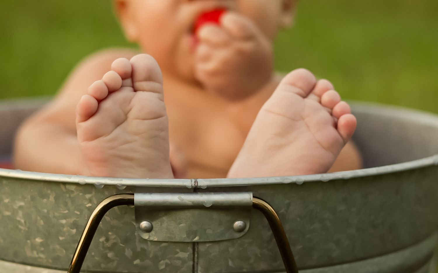 Close-up of a baby's feet propped on the edge of a galvanized tub.