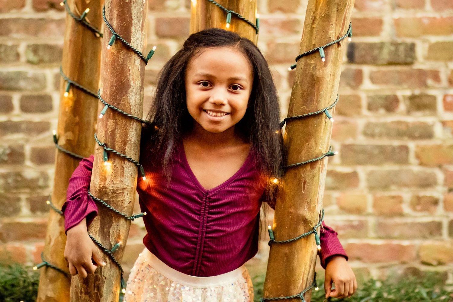 Smiling young girl standing between bamboo poles wrapped in string lights.