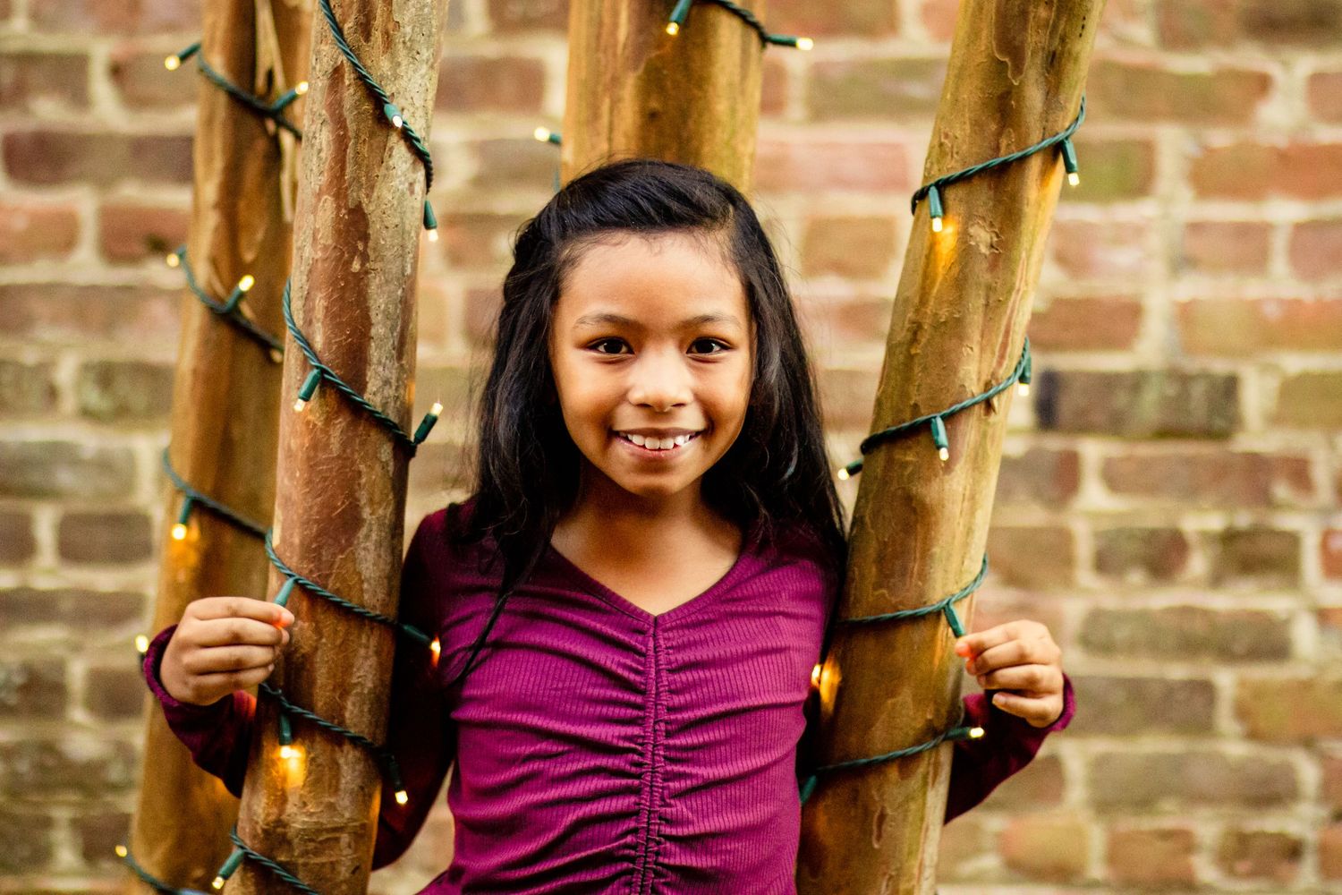 Young girl smiling while holding bamboo poles with fairy lights outdoors.