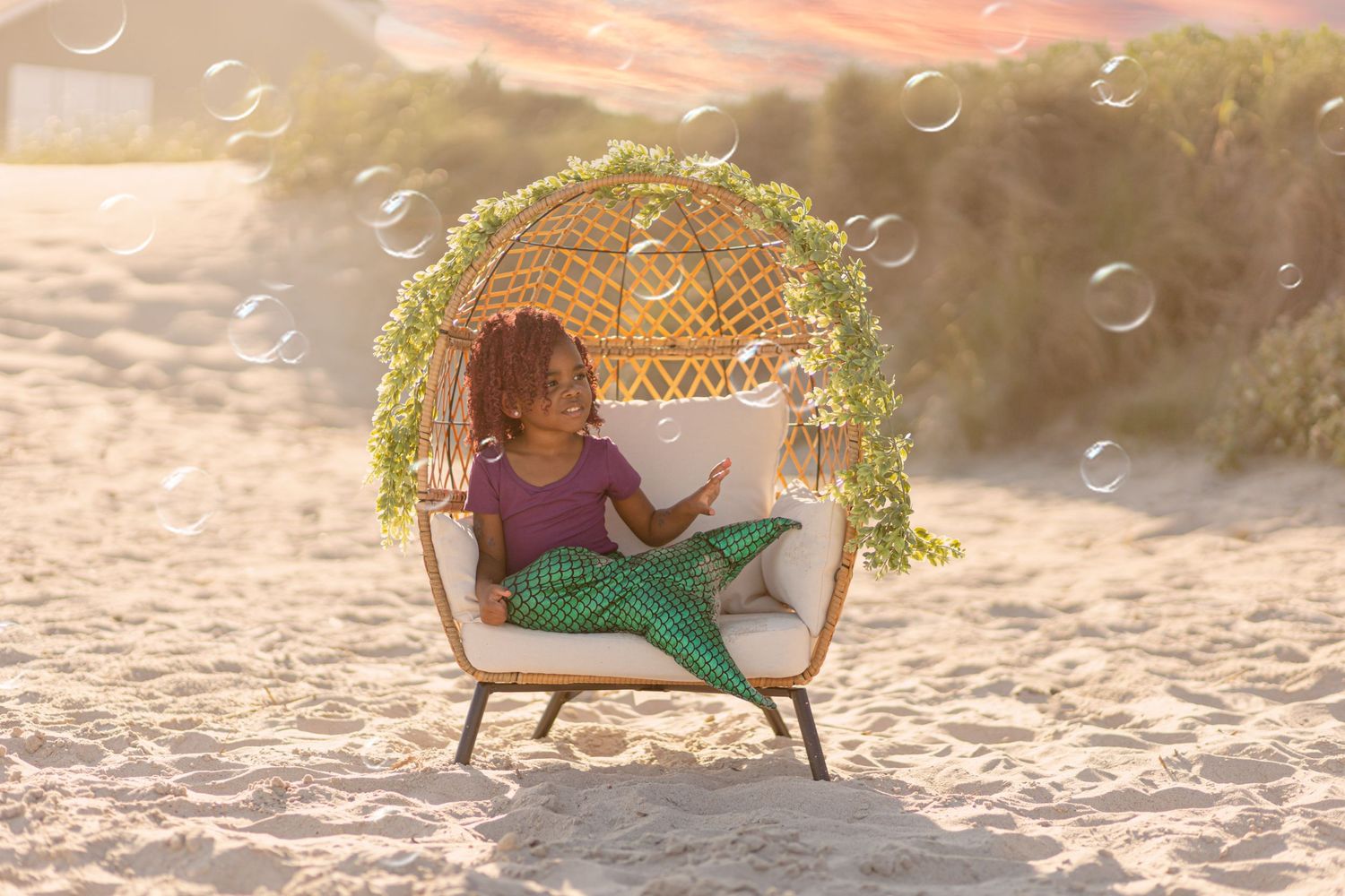 Young girl in mermaid costume relaxes in wicker beach chair surrounded by bubbles.