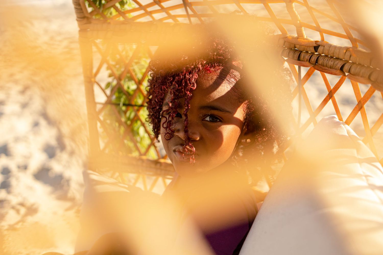 Close-up view of a young girl's face seen through the woven gaps of a rattan chair.
