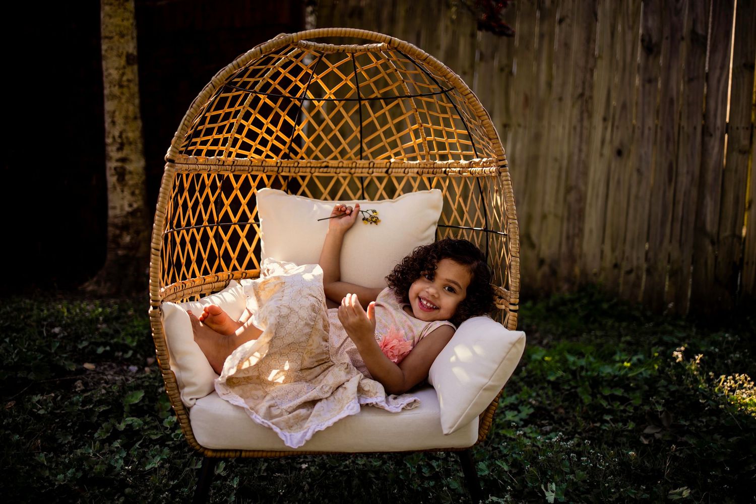 Little girl lying back comfortably in a wicker egg chair in a garden.