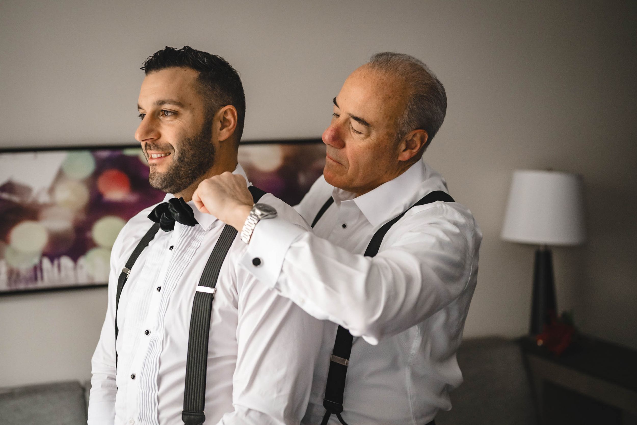 Wedding preparation scene showing formal attire adjustments in natural light.
