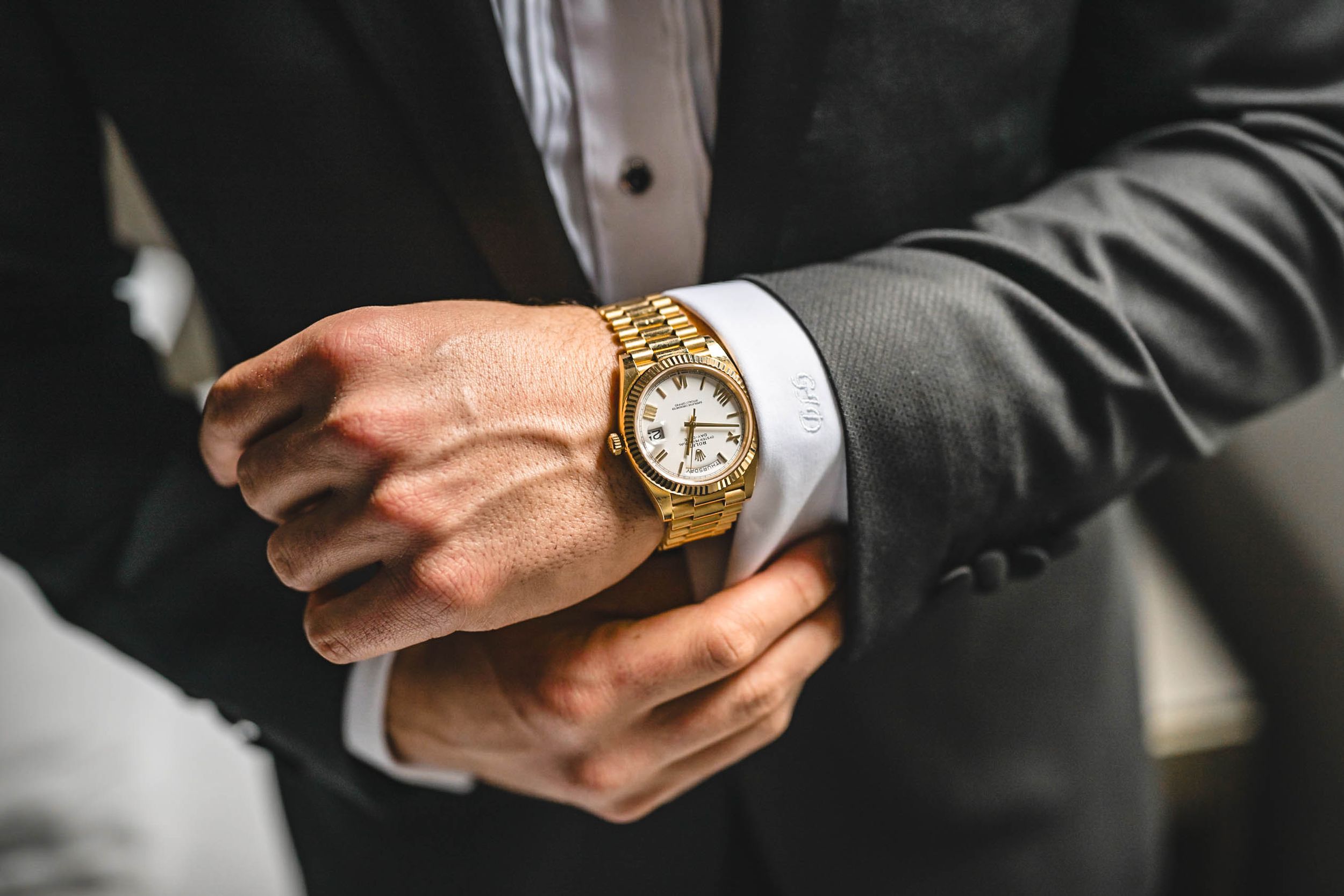 Close-up of hands adjusting a gold watch with formal suit cuff and sleeve visible.