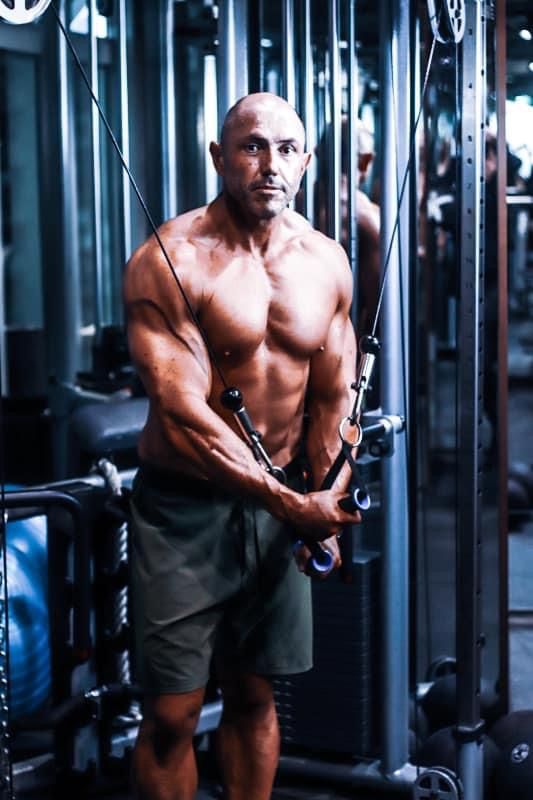 Muscular bald man doing cable crossover exercise shirtless in a professional gym.
