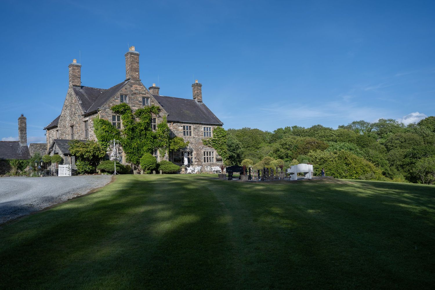 Stone manor house with chimneys set on sprawling green lawn under blue sky.
