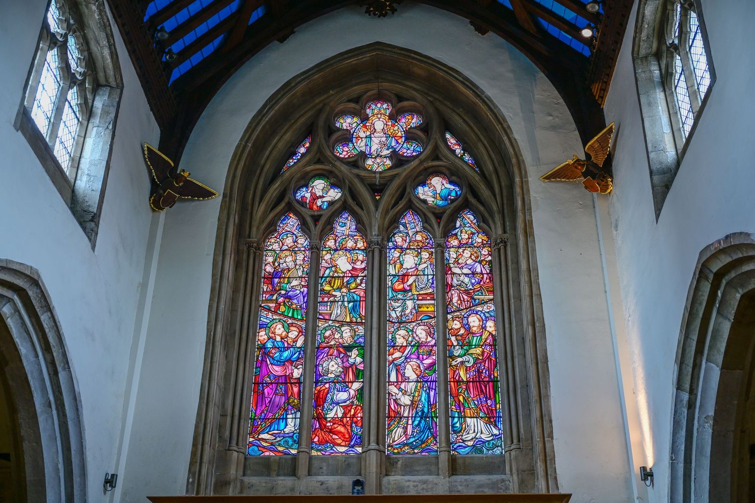 Vibrant stained glass church window with religious scenes and Gothic architectural framing.