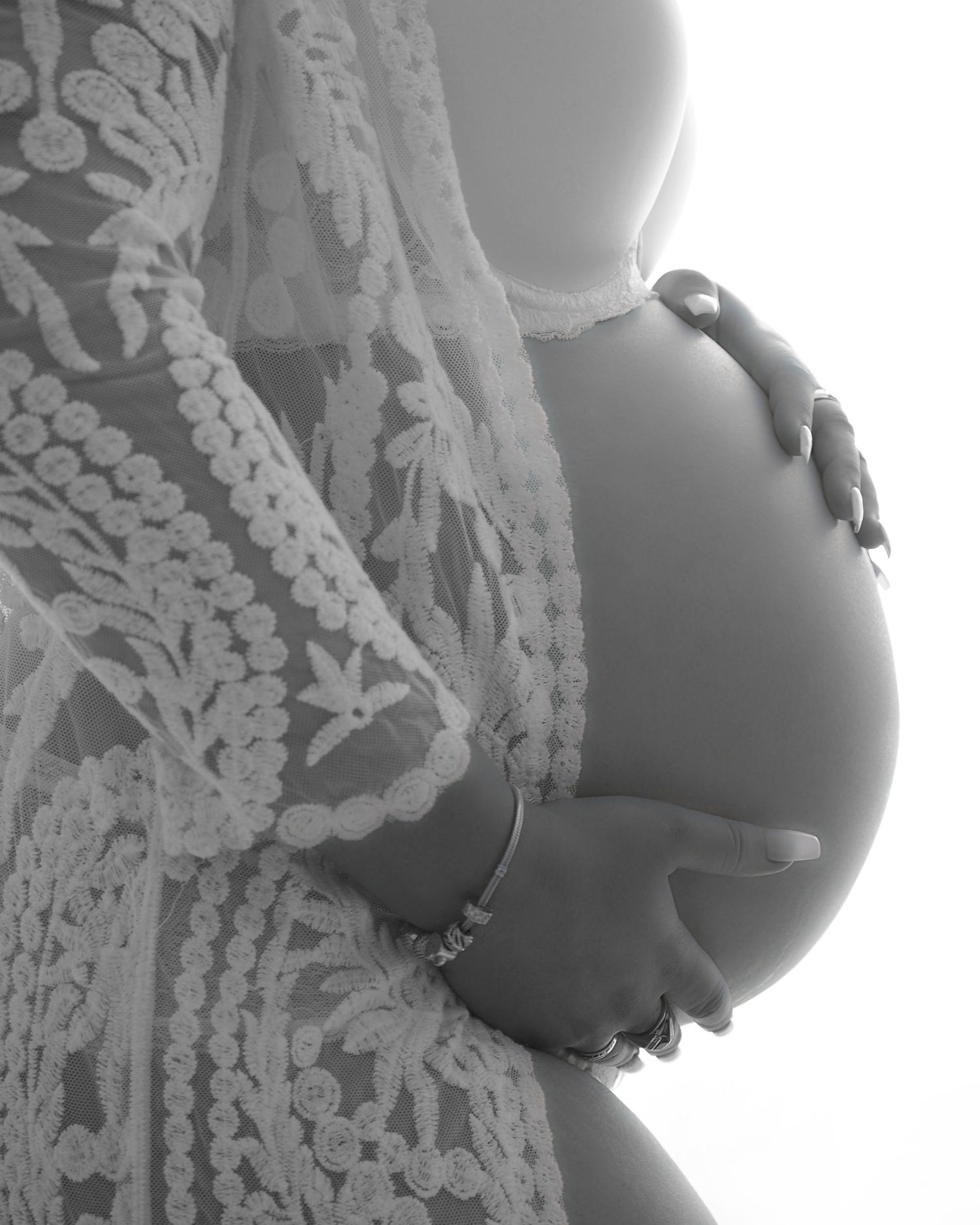 a pregnant stomach of a female lady holding her stomach wearing a white lace jacket
