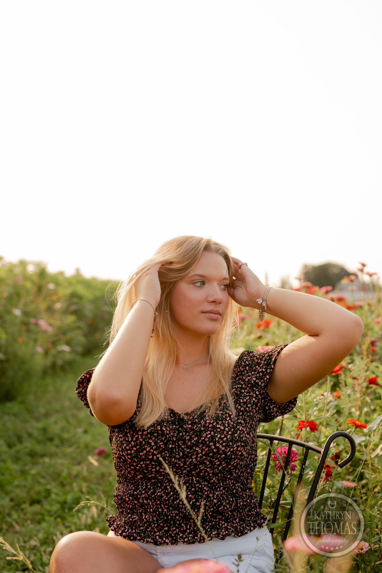 Portrait in a sunlit wildflower field wearing a floral top with long blonde hair blowing in the breeze.