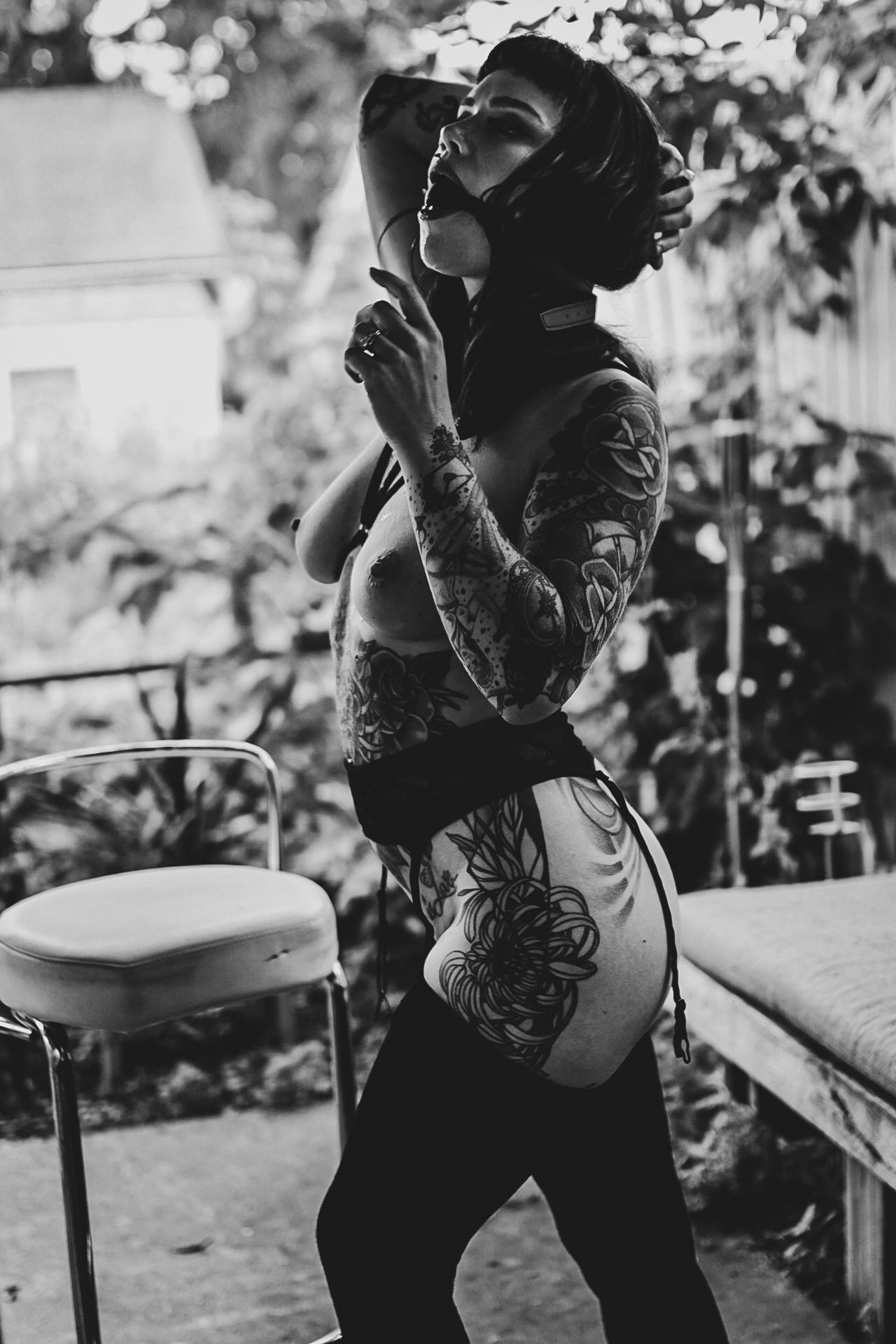 Black and white portrait of tattooed figure in artistic outdoor setting.