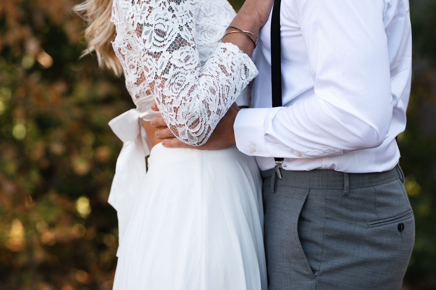 Close-up detail of a bride and groom embracing, showing lace dress details.
