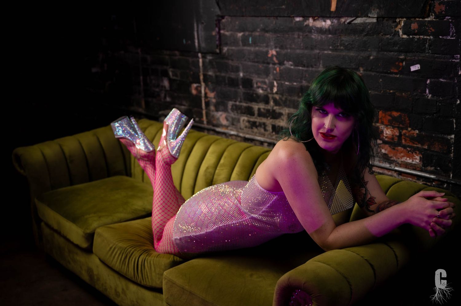A model stretched out on a green coached, bathed in pink light