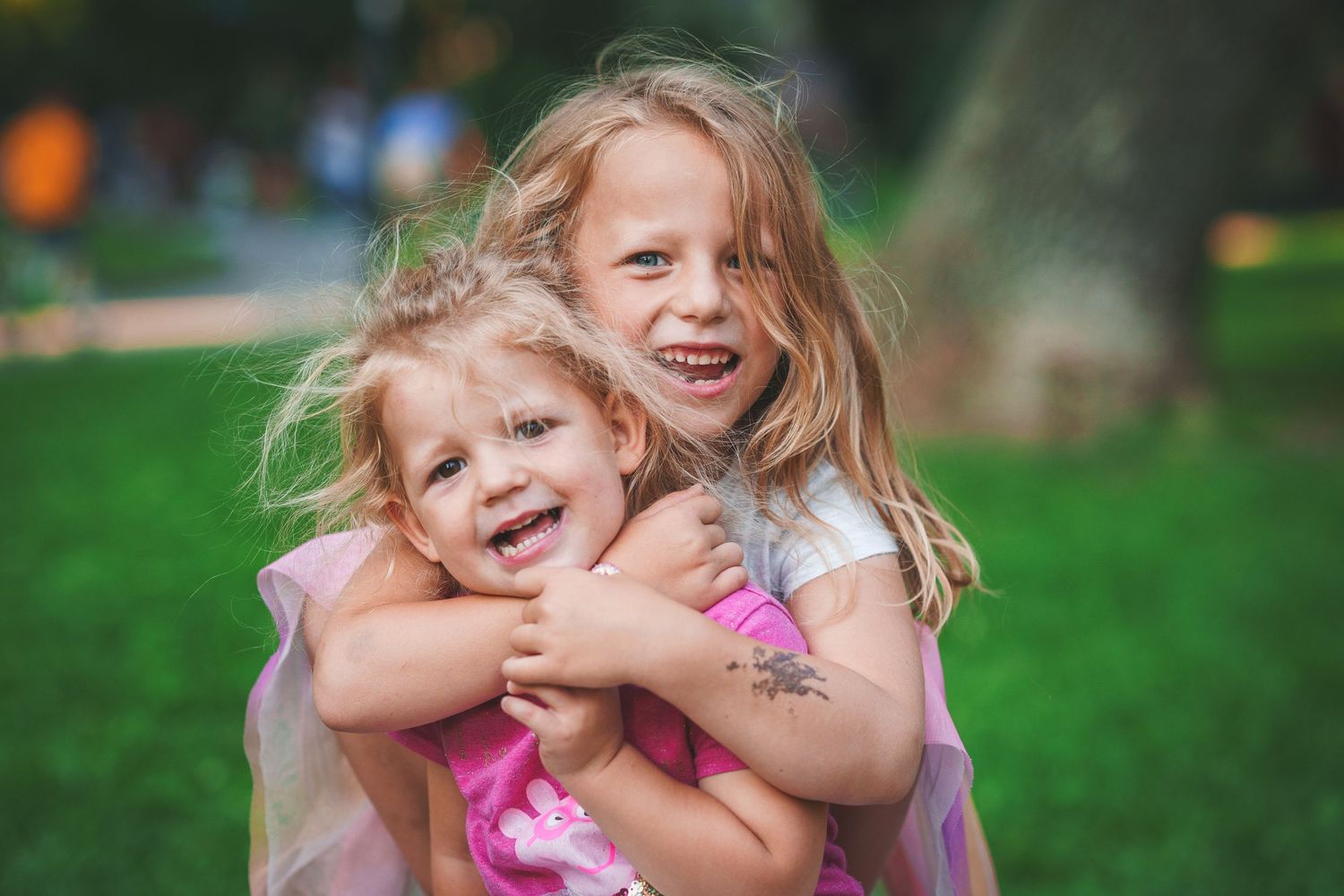 Two joyful children embracing and laughing together on green grass during a sunny day.