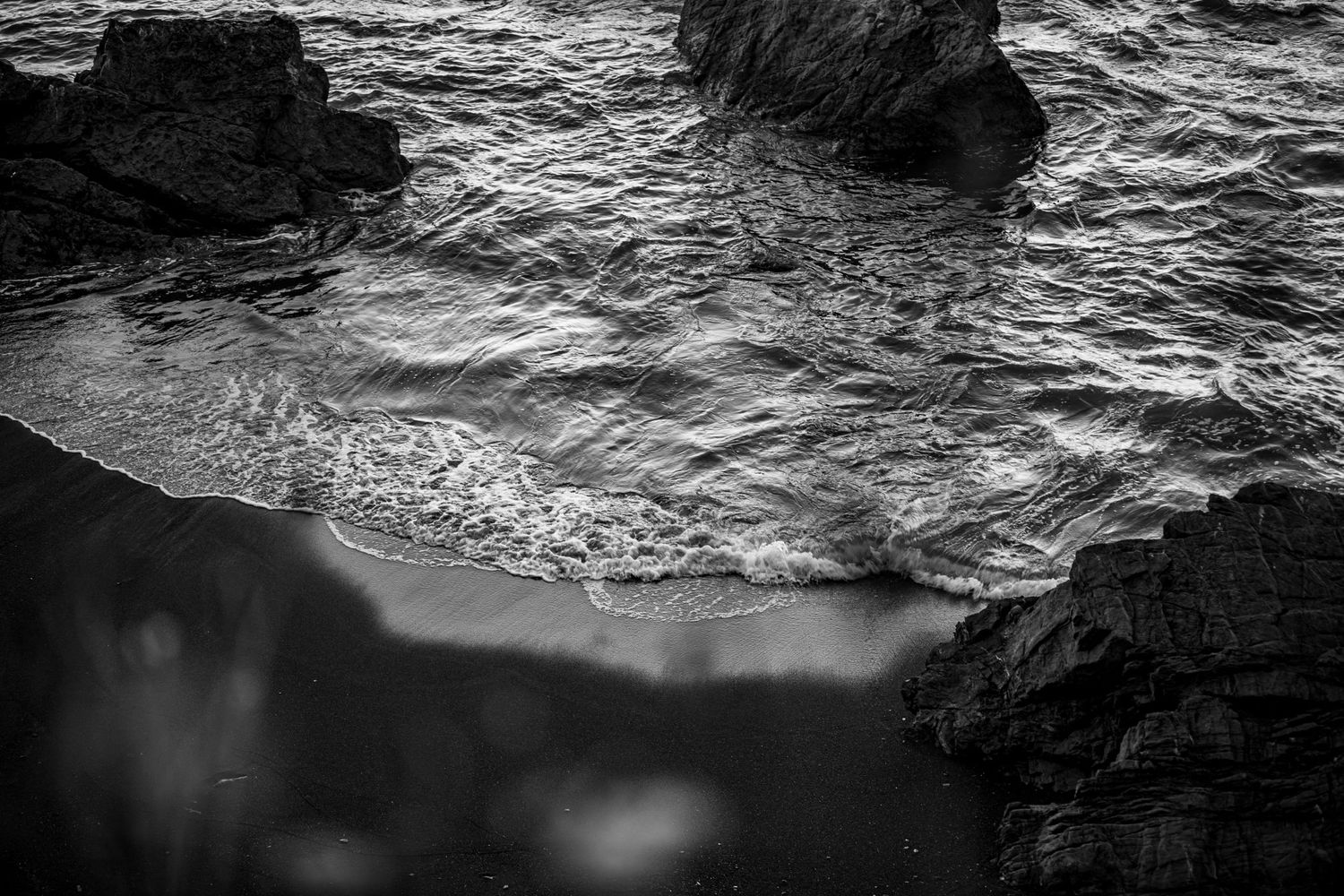 Abstract black and white underwater photograph showing rock formations and rippling water surface.