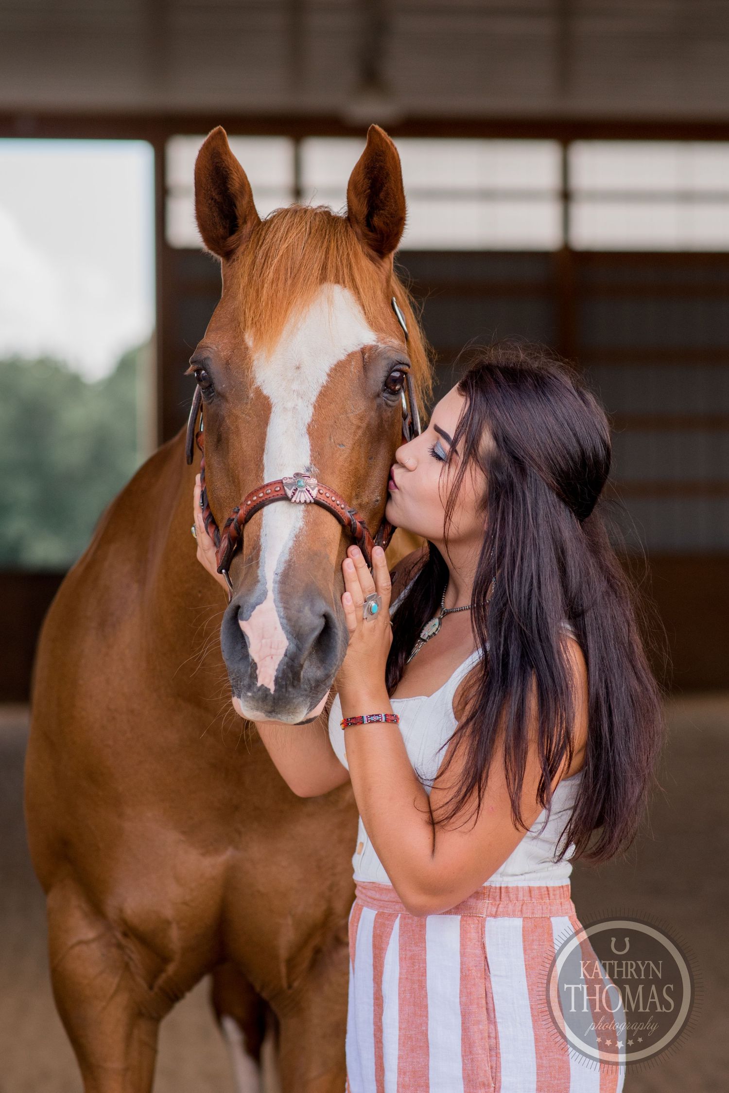A chestnut horse with white blaze receives affection in a stable setting.
