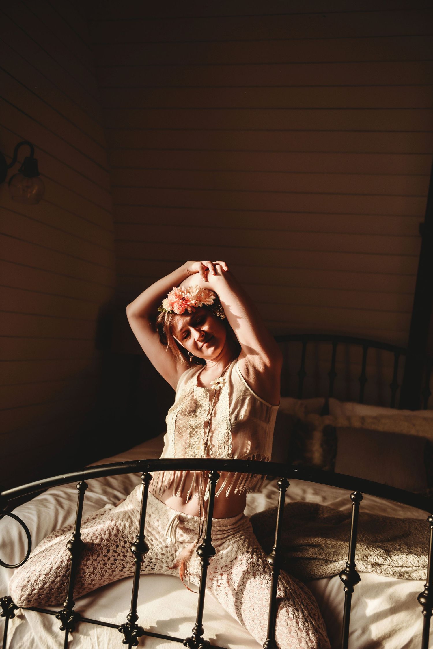 Woman stretching in a sunbeam on a farmhouse style bed wearing flowers in her hair