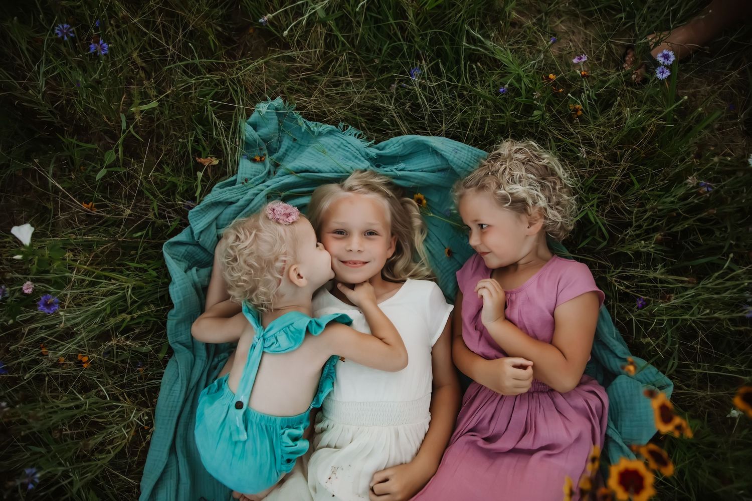 Children laying on teal blanket playing and giggling together in tall grass.