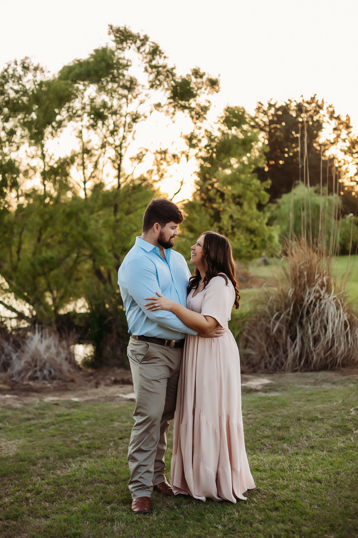 Couple embracing in romantic sunset portrait session with trees in background.