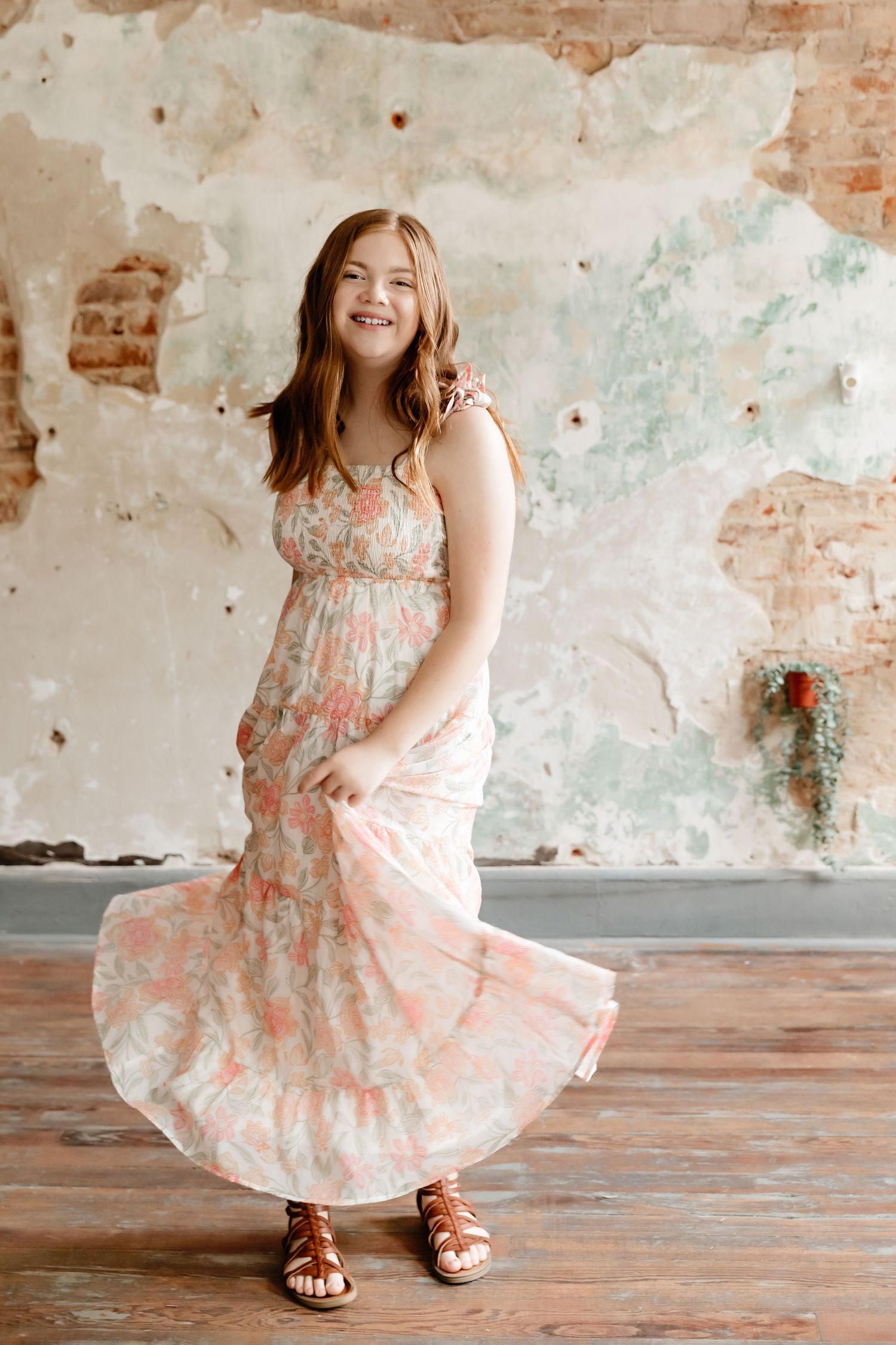 Young person twirling in floral dress against distressed wall background.