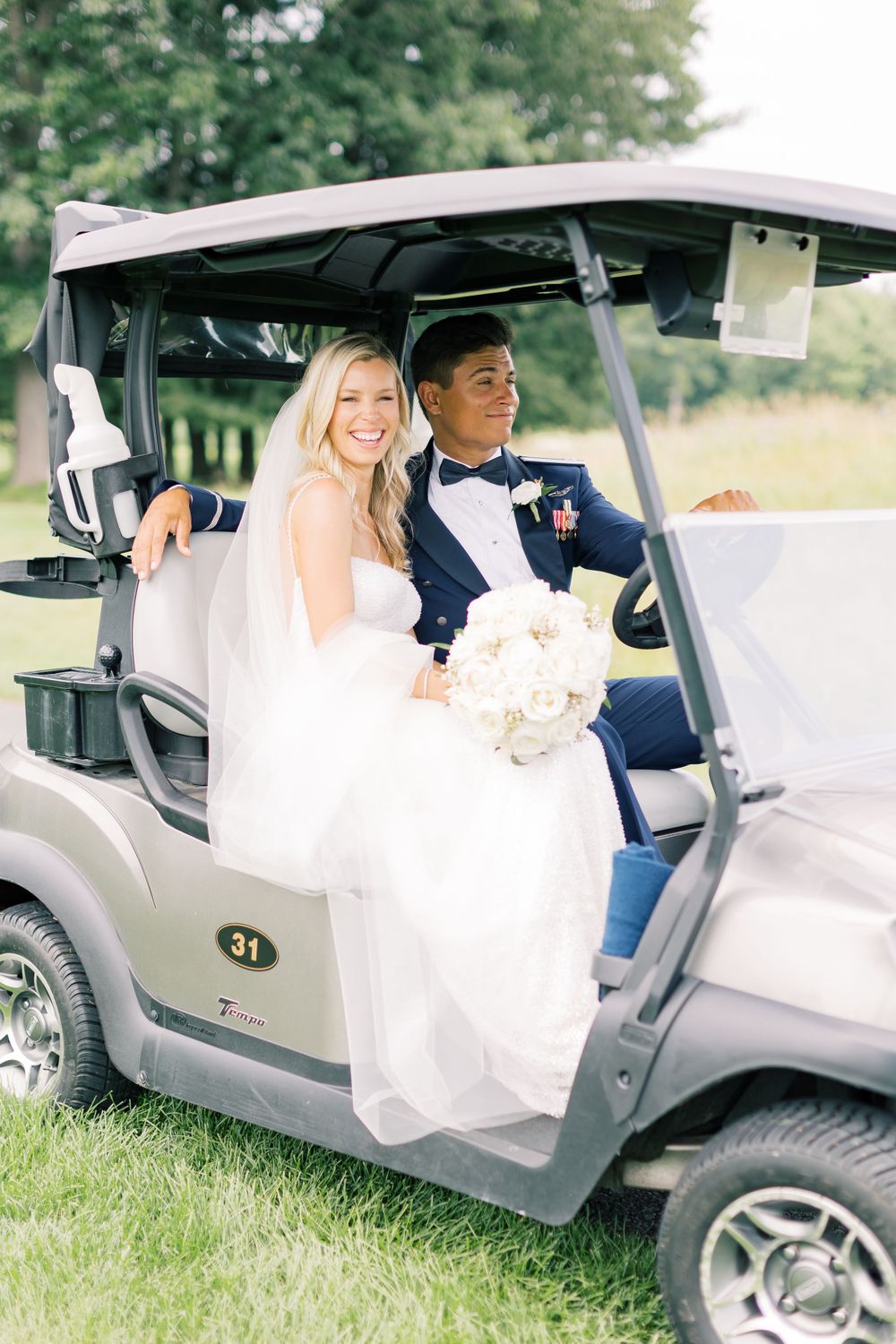 Newlyweds riding in a golf cart on their wedding day through a lush green setting.