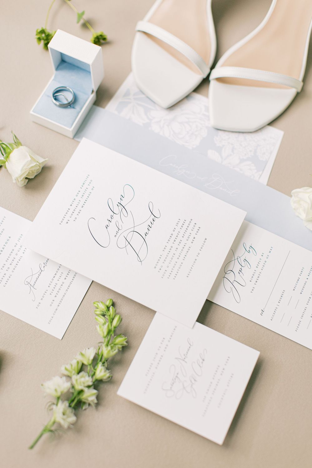 Wedding details featuring white invitation suite, heels, ring box and delicate floral accents.