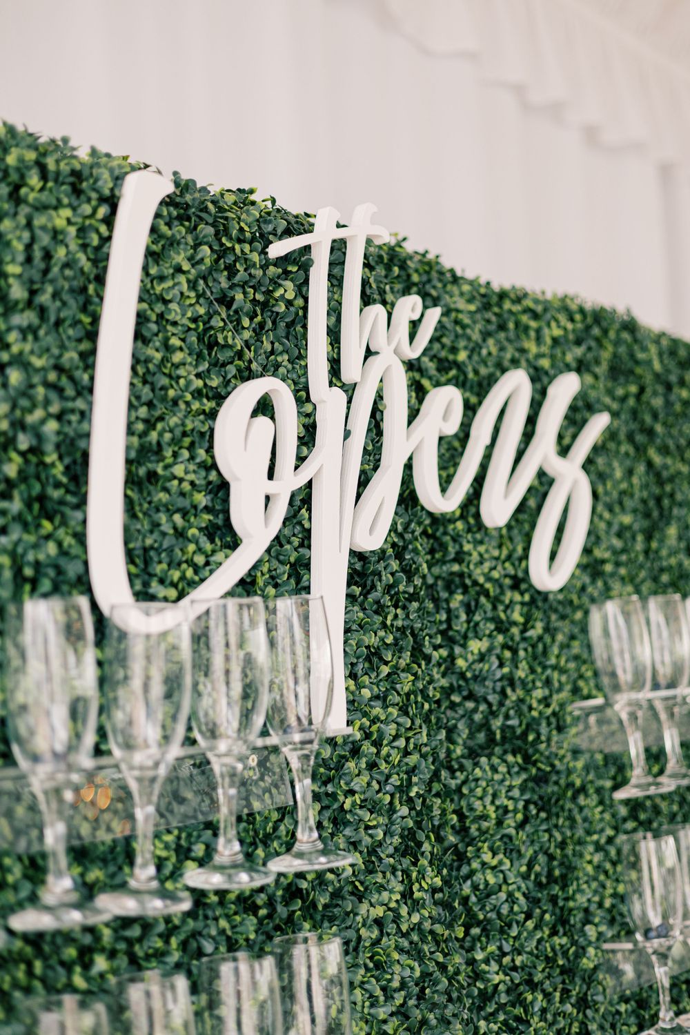 Decorative 'Cheers' sign mounted on green hedge wall with champagne flutes.