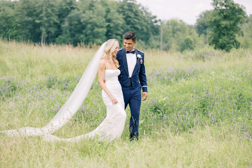 Wedding couple standing in a dreamy meadow with flowing veil and navy suit.