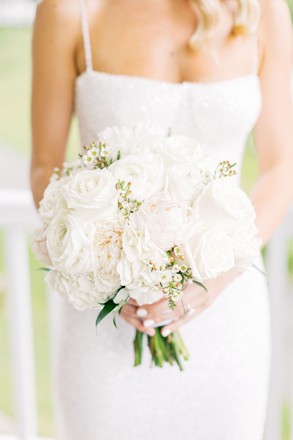 A stunning white bridal bouquet with roses and delicate florals against a white dress.
