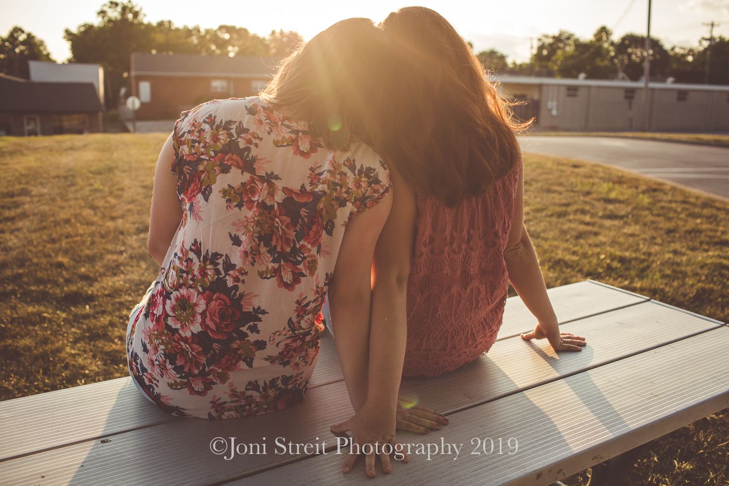 Friends in floral and pink tops sitting together during sunset.