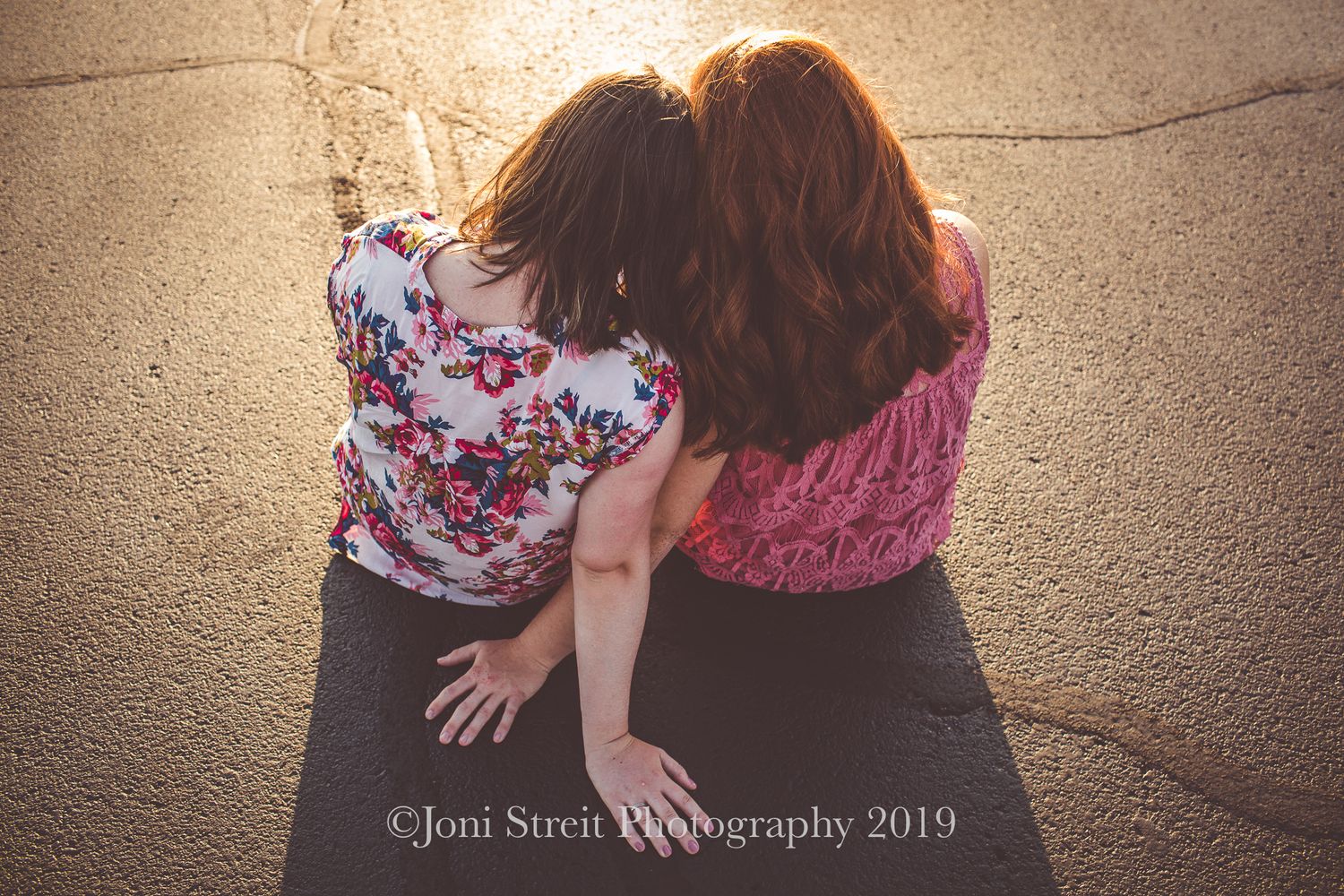 Friends in floral and pink tops sitting close together on a warm day.