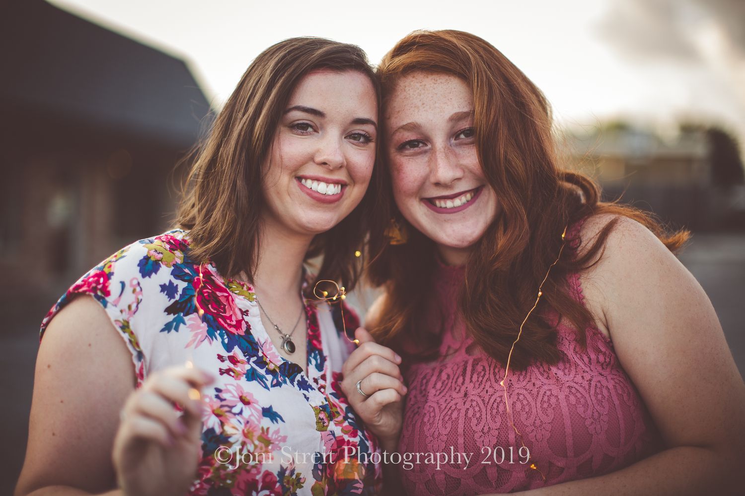 Friends in floral and pink tops laughing together during golden hour.