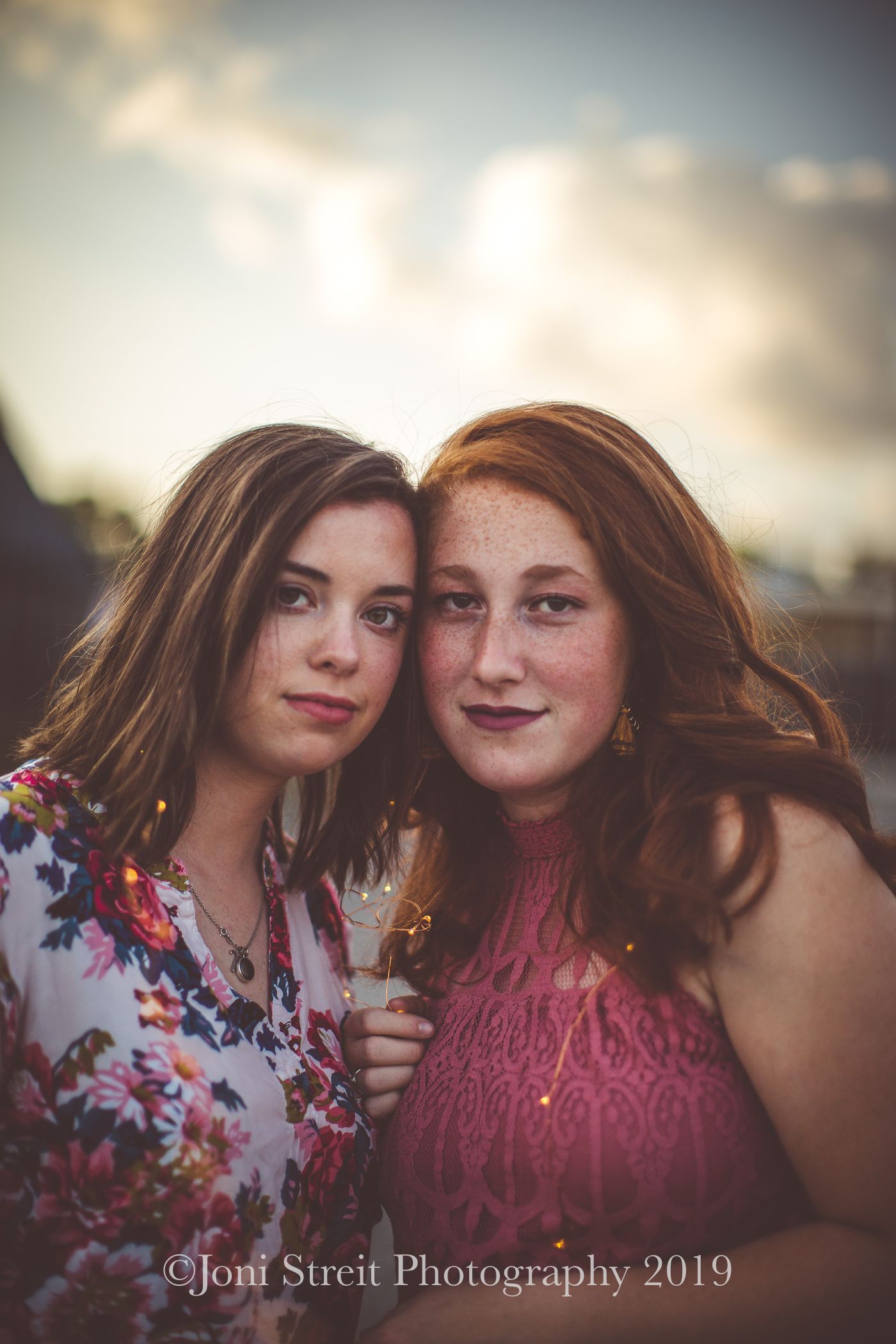 Close portrait of two friends against a soft sunset sky.