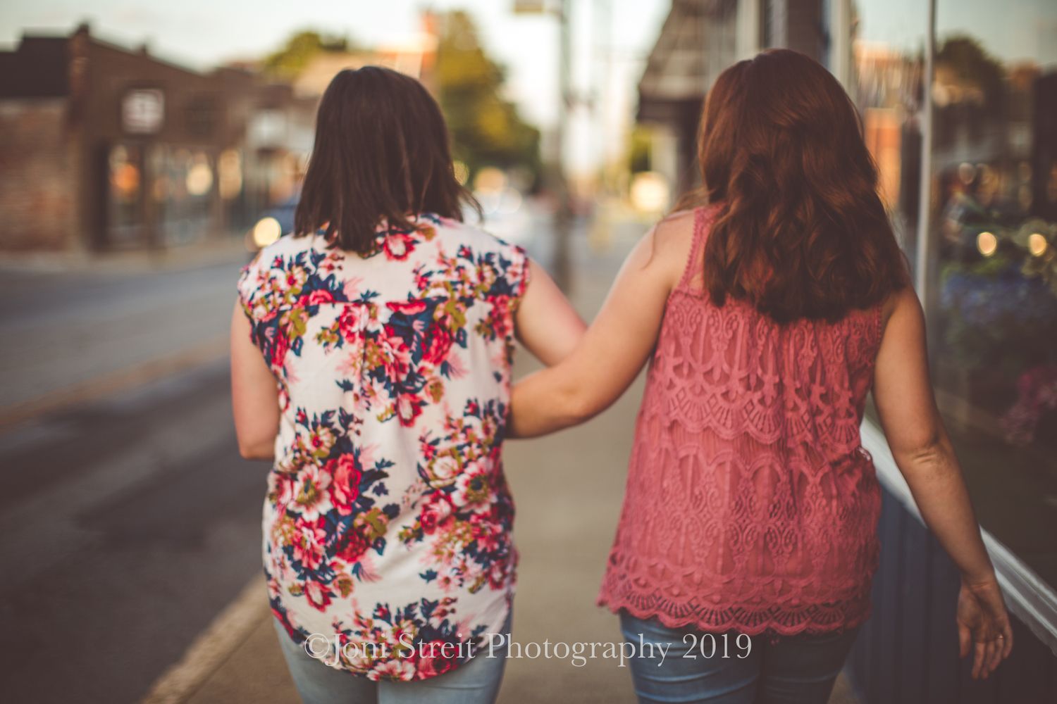 Friends walking together down a street at sunset, wearing floral and pink tops.