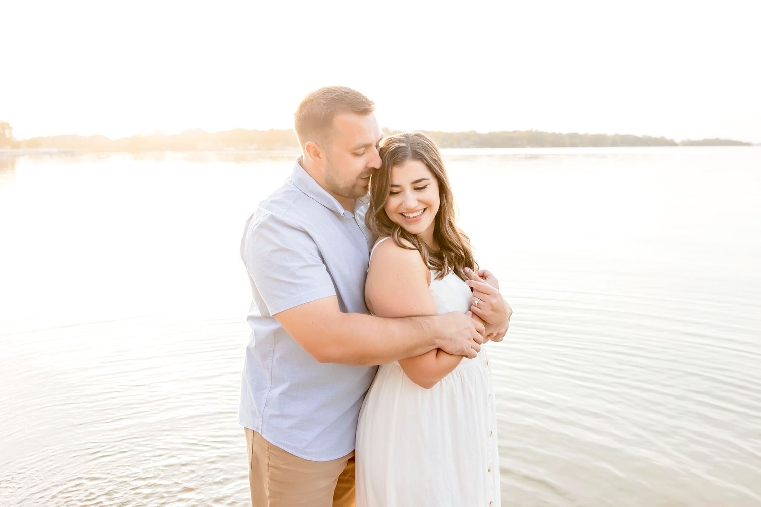Romantic couple embrace by lake at sunset during outdoor photo session.