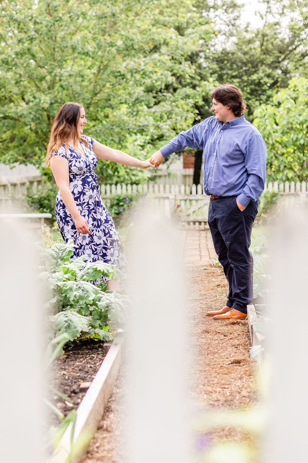 Couple holds hands while standing on garden path surrounded by greenery.