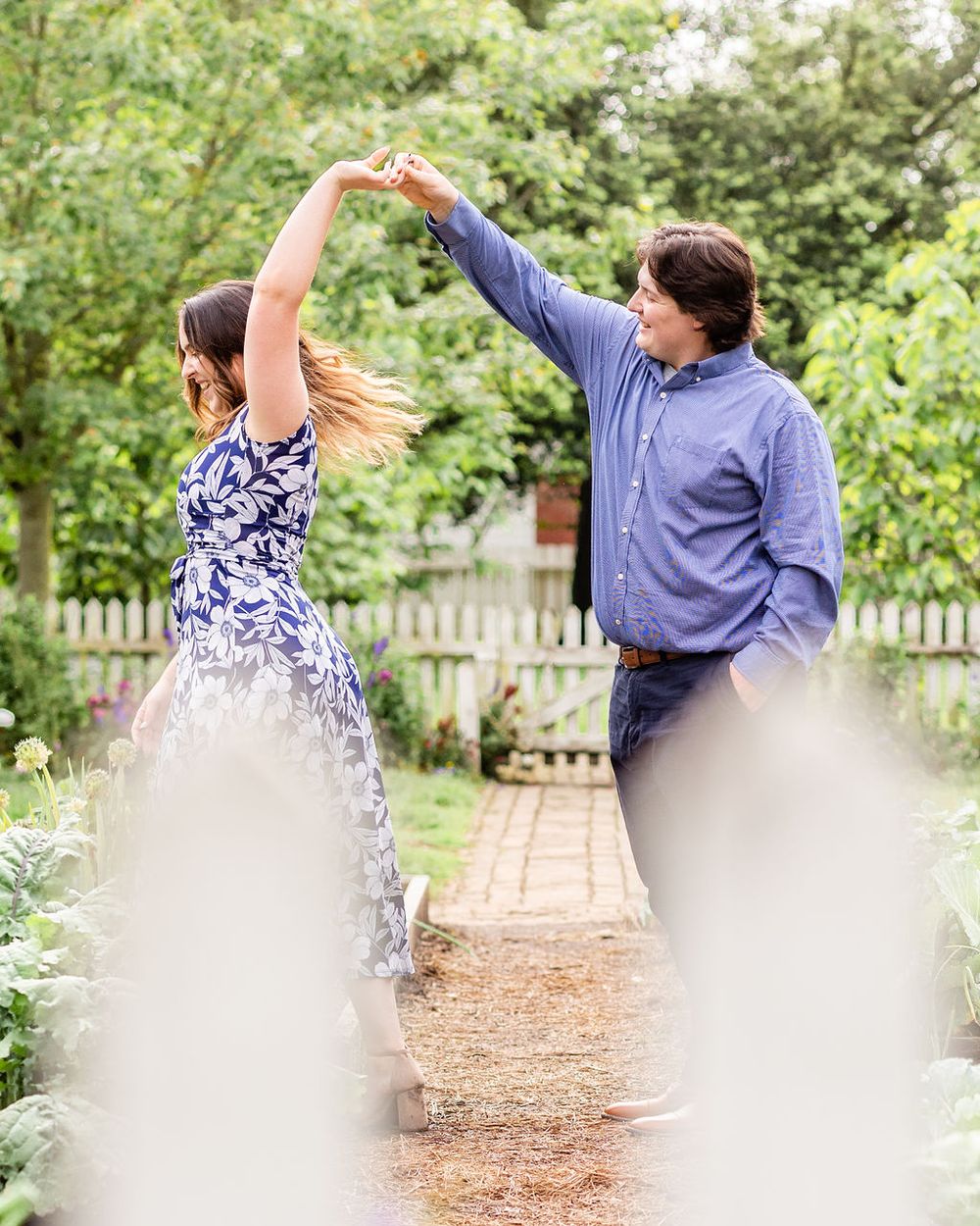 Couple dances together on garden path with decorative fence in foreground.