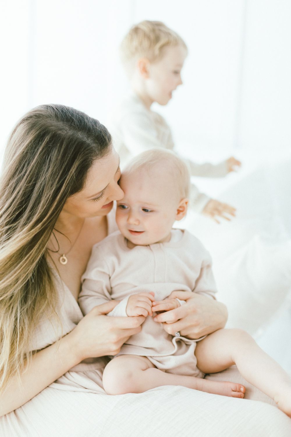 Family moment showing tender interaction on white bedding in bright room.